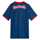 Vista  traseira da Camisa Away do Red Bull Bragantino 2025-2026, cor azul marinho. Apresenta um padrão geométrico radiante em azul cyan. A gola V e os punhos das mangas são vermelhos. Frente com escudo do clube, logos da Puma e patrocínio central Red Bull. Costa com "REDBULL BRAGANTINO", o nome "MASSA BRUTA" e o número "25" em branco.