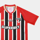 Camisa oficial reserva (Away) do São Paulo FC 2025/26, versão Torcedor, da New Balance. A peça exibe as icônicas listras verticais vermelhas, pretas e brancas com cores profundas e nítidas. Apresenta gola redonda preta com detalhes em dourado metálico, que também decoram as bordas das mangas. O escudo do clube é aplicado em patch bordado de alta definição no lado esquerdo, contrastando com o logo da marca em dourado à direita. O tecido possui uma trama respirável e toque macio, ideal para o uso casual de al