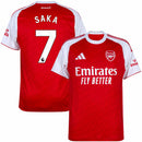 Camisa de futebol autêntica do Arsenal modelo Home para a temporada 2025-2026 da Adidas. A visão geral apresenta o corpo em vermelho vibrante com um padrão de monogramas texturizados e mangas curtas brancas. Na frente, destacam-se o escudo bordado do Arsenal, o logo da Adidas em branco e o patrocinador "Emirates Fly Better". Os ombros exibem as três listras clássicas em vermelho. A visão posterior (costas) revela a personalização premium com o nome "SAKA" e o número "7" em branco oficial. O tecido é leve e 