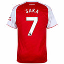 Camisa de futebol autêntica do Arsenal modelo Home para a temporada 2025-2026 da Adidas. A visão geral apresenta o corpo em vermelho vibrante com um padrão de monogramas texturizados e mangas curtas brancas. Na frente, destacam-se o escudo bordado do Arsenal, o logo da Adidas em branco e o patrocinador "Emirates Fly Better". Os ombros exibem as três listras clássicas em vermelho. A visão posterior (costas) revela a personalização premium com o nome "SAKA" e o número "7" em branco oficial. O tecido é leve e 