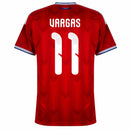Visão Geral e Detalhes: Foto frontal da Camisa da Seleção do Chile Home 2026 vermelha, destacando o número 11 do atacante Eduardo Vargas. O texto alternativo descreve o padrão de tecido em zigue-zague, o escudo oficial da ANFP, as listras brancas nos ombros e a gola azul e branca. Inclui a visão das costas com a personalização "Vargas 11" e detalhes do tecido tecnológico, utilizando os termos: "Camisa Chile Vargas 11", "Nova Camisa do Chile 2026" e "Uniforme Chile Adidas Vermelho".