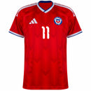 Visão Geral e Detalhes: Foto frontal da Camisa da Seleção do Chile Home 2026 vermelha, destacando o número 11 do atacante Eduardo Vargas. O texto alternativo descreve o padrão de tecido em zigue-zague, o escudo oficial da ANFP, as listras brancas nos ombros e a gola azul e branca. Inclui a visão das costas com a personalização "Vargas 11" e detalhes do tecido tecnológico, utilizando os termos: "Camisa Chile Vargas 11", "Nova Camisa do Chile 2026" e "Uniforme Chile Adidas Vermelho".