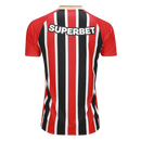 Camisa oficial de jogo (versão Jogador) do São Paulo FC 2025/26 New Balance. A peça exibe as tradicionais listras verticais em vermelho e preto, separadas por finas linhas brancas, com cores vibrantes e acabamento fosco. O escudo do clube e o logo da marca são aplicados em relevo emborrachado (heat-transfer) para maior leveza. A modelagem é visivelmente ajustada (slim fit), com gola em "V" adornada por detalhes dourados sutis, transmitindo uma estética de alta performance e sofisticação técnica.