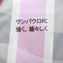 Camisa oficial de jogo (versão Jogador) do São Paulo FC 2025/26 New Balance. A peça exibe as tradicionais listras verticais em vermelho e preto, separadas por finas linhas brancas, com cores vibrantes e acabamento fosco. O escudo do clube e o logo da marca são aplicados em relevo emborrachado (heat-transfer) para maior leveza. A modelagem é visivelmente ajustada (slim fit), com gola em "V" adornada por detalhes dourados sutis, transmitindo uma estética de alta performance e sofisticação técnica.